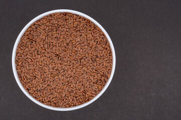 Linen seeds in a white glass bowl. Top view photo of linen seeds on dark grey background. Isolated close up photo