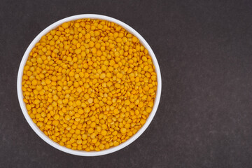 Yellow lentils in a white glass bowl. Top view photo of lentils on dark grey background.