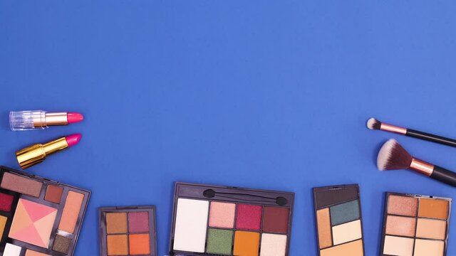 Eye shadow palettes and brushes moving on bottom of dark blue background. Stop motion flat lay