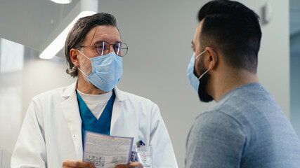 Mature doctor in mask giving prescription to patient