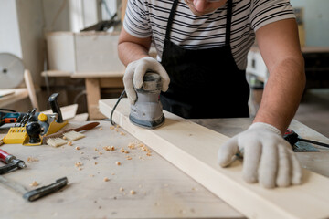 Man worker using electric sander in workshop. Joiner sanding wooden board on table.  Carpentery work. Small Business Concept