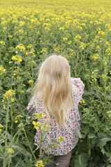 Outdoor candid portrait of cute blonde girl in field of yellow flowers.