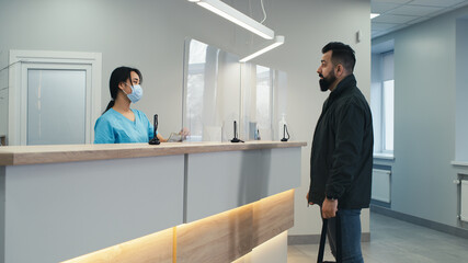 Fototapeta premium Bearded patient communicating with doctor and nurse on reception