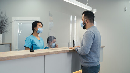 Man in mask speaking with nurse on hospital reception