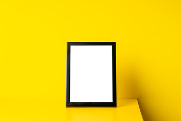 blank picture frame mockup on yellow desk over yellow wall. creative greeting card template