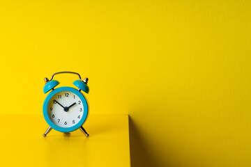 blue alarm clock on a yellow desk and yellow wall background. copy space. abstract time concept