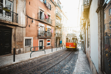 Plakat A wide-angle view of a red retro tram on a narrow street with one-way rail traffic in a European city; a vintage tourist streetcar in red and yellow colors on a tramway track over paving stone, Lisbon