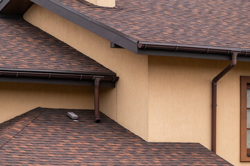 part of the house close-up, roof waterproofing, brown tile roof with gutters © Andrey