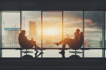 Two business partners sitting in front of each other on elegant armchairs: a businessman with a...