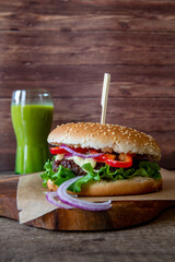 Freshly made burger on the cutting board on the wooden table and a green smoothie in the background, with copy space, vertical photo