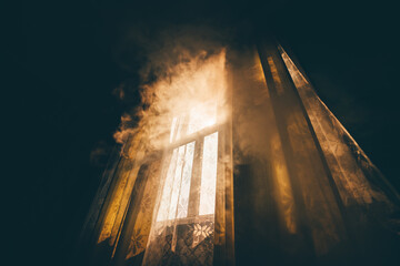 A wide-angle mysterious view from a dark room on a smoke-shrouded window lit by morning or evening sun illuminating the smoke with warm light and casting shadows on the tulle and curtains