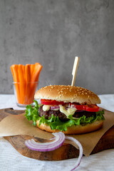 Delicious grilled homemade burger with beef, tomato, onion, cucumber and lettuce and carrot sticks in the background, with copy space