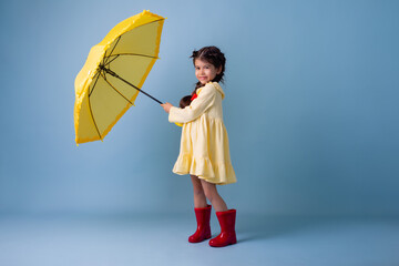Happy cute little Girl Indian in red rubber boots, cotton dress holds in her hands yellow umbrella...