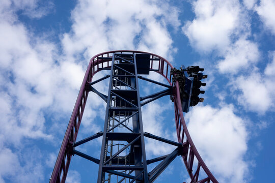 Roller-coaster Ride In An Amusement Park Against Blue Sky And Clouds.