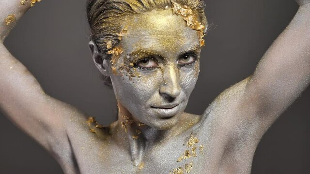 Beautiful young female model with gold and silver paint on her skin and hair in the studio.