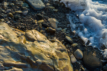 pebble stones on the sea beach, the rolling waves of the sea with foam