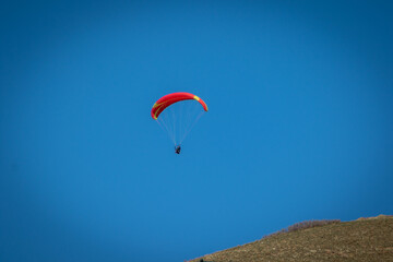 Fototapeta na wymiar Paraglider With Red Parachute Wing Flying in a Blue Sky With Clouds
