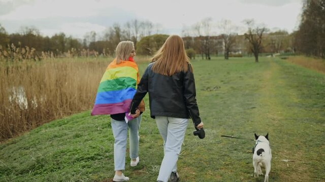 Backside: Female LGBT couple walking with french bulldog in park