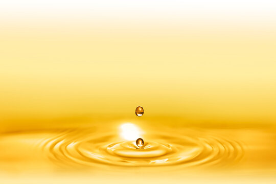Macro shot of droplets splash of a golden elixir for beauty and body care creating circular waves by falling down on the shining liquid.