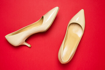 Classic beige patent leather pumps or shoes with low kitten heels on red background.