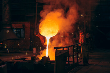 Metallurgical plant, hot liquid metal pouring into special mold in foundry with worker.