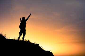 silhouette of a motivated person on the top of mountain celebrating with fist up to the sky. 