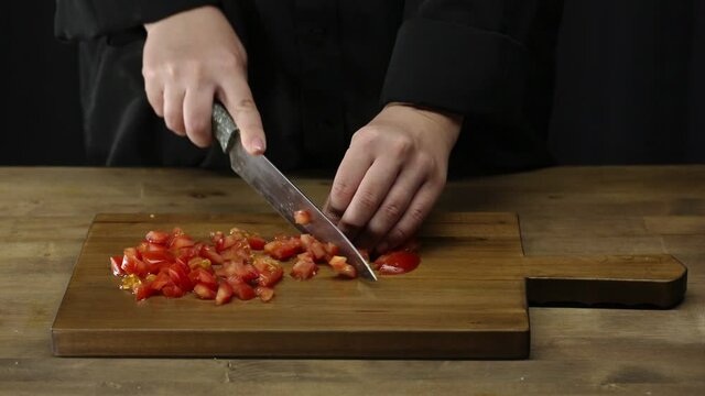 Women's hands use a kitchen knife to cut a fresh tomato on a wooden chopping board. Healthy eating. Sliced tomato. Preparation of salad ingredients.