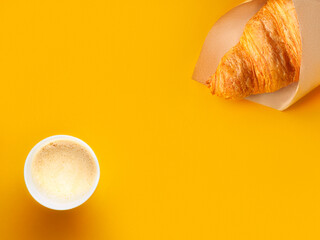 Flat lay of paper cup of coffee and croissant in craft paper on bright orange paper background. Breakfast concept. Minimalism. Copy space.