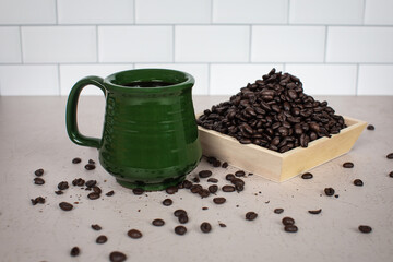 Green coffee mug filled with brewed coffee with dark roasted coffee beans piled up in wood bowl and scattered 