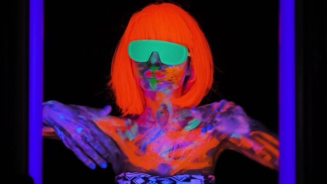 Beautiful model woman in wig and glasses with colorful bright fluorescent makeup in neon light, nightclub disco.