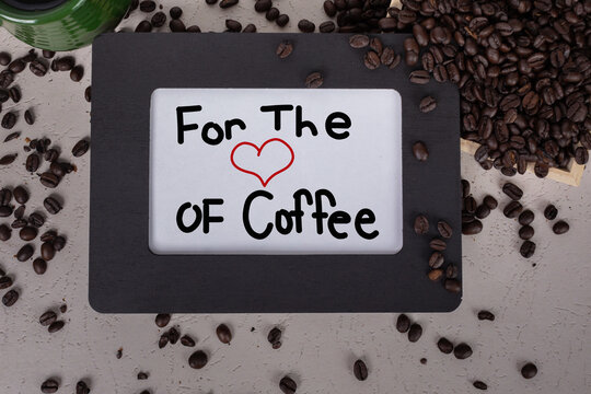 For the love of coffee sign with red heart in black picture wood frame whole coffee beans scattered around with green ceramic coffee mug filled with dark coffee