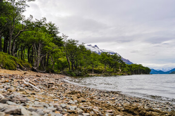 beach of rocks in serene lake and snowy mountains background