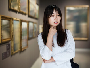Chinese serious positive glad female visitor looking at artwork painting in the museum indoors