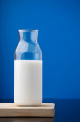 transparent glass milk bottle, on wood, blue background