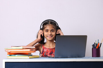 Little girl studying online using her laptop or computer at home.