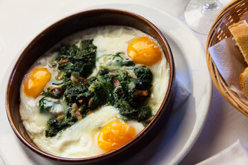 Traditional Catalan fried eggs with spinach, raisins and ham served in clay bowl