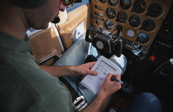 Crop focused pilot ticking in checklist in airplane