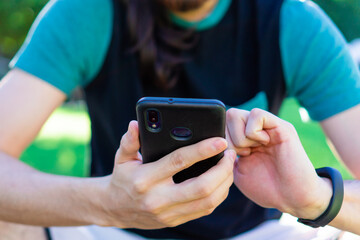 hands of a man sitting in a park using his smart phone