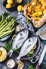Fresh uncooked dorado or sea bream fish with lemon ,asparagus, herbs, olive oil and spices over...