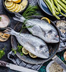 Fresh uncooked dorado or sea bream fish with lemon ,asparagus, herbs, olive oil and spices over...