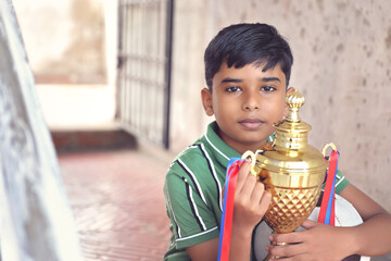 Indian school boy holding a golden trophy cup	