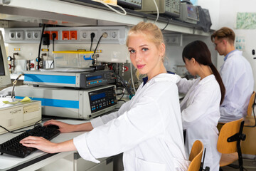 Portrait of young female lab technician engaged in research in chemical laboratory with her colleagues