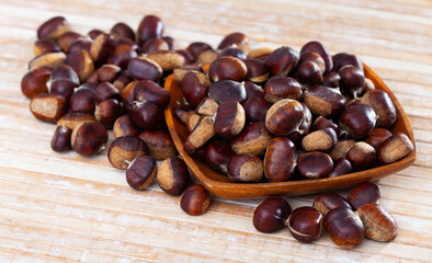 Obraz premium Pile of raw edible chestnuts in wooden bowl on table. Cooking of popular street food