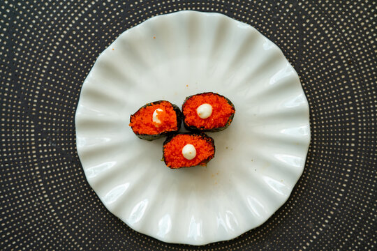 Salmon eggs or Ikura in Japanese style sushi fresh from raw salmond fish served on a white plate on dark background.