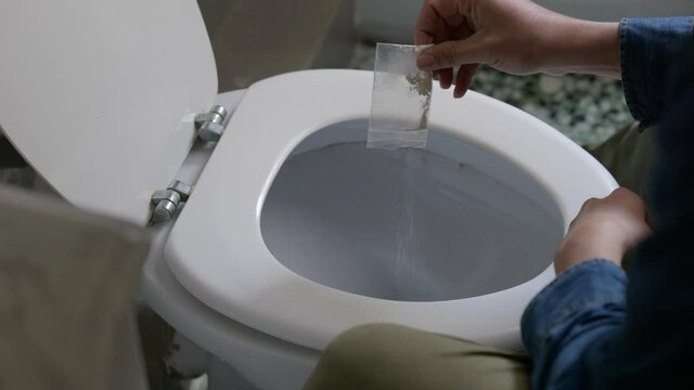 Male pouring white powder narcotics drug substance in plastic zip lock back down toilet