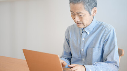 ノートパソコンの前で困惑するシニア男性