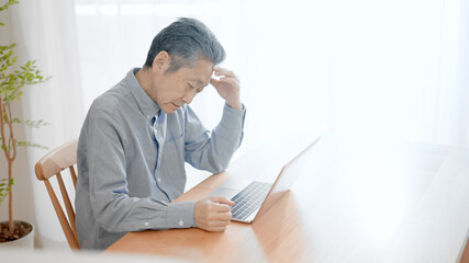 ノートパソコンの前で困惑するシニア男性