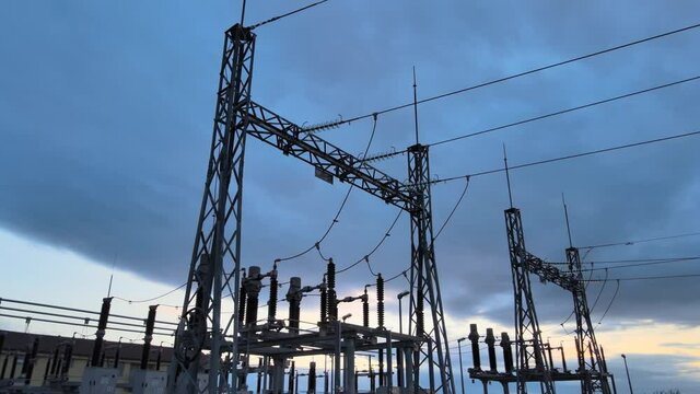 Panning shot showing electrical distribution network comprising of powerlines between electrical towers at substation.