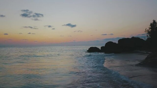 Bermuda drone shot of sunset at West Whale Bay Park with waves cresting onto a white sandy beach and rock formations
