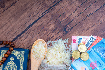 Holy Al Quran, Coins, Banknotes and Rice on wooden background. Zakat concept. Zakat is a form of alm-giving as a religious obligation